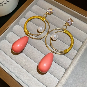 Dettaglio orecchini dorati con filo di seta giallo, perle e pendenti in resina rosa corallo