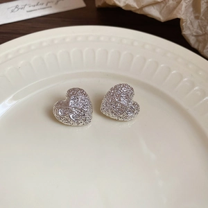 Detailed view of silver heart-shaped stud earrings with bow relief on a ceramic dish