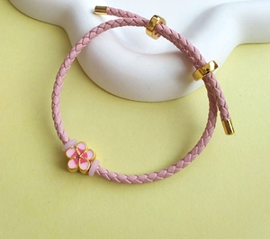 Close-up of pink braided leather bracelet with golden flower pendant and adjustable slide
