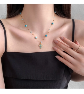 Detail of cross pendant necklace with blue beads and gold plating on a model's neck