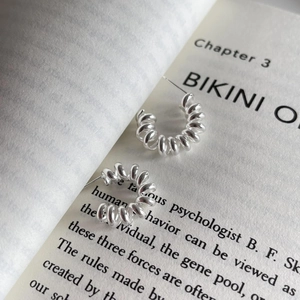 Detailed view of minimalist silver spring earrings displayed on an open book background