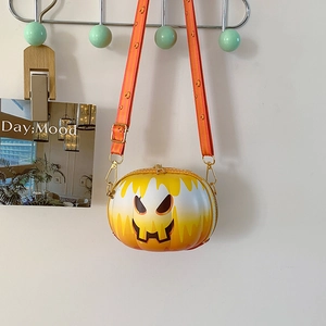 Detail of orange pumpkin face crossbody bag with zipper and patterned strap on wall hook