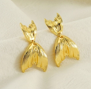 Vue détaillée des boucles d'oreilles queue de poisson dorées avec texture sur tissu doux