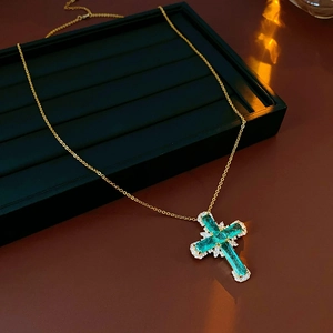 Macro view of golden cross pendant with green gemstone and sparkling zircons