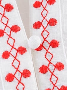 Macro detail of red flower embroidery and cloth button on white cotton linen shirt