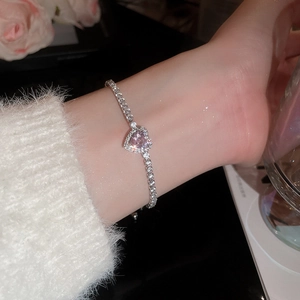 Close-up of heart-shaped pink diamond bracelet on wrist with elegant rose background
