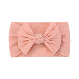 Soft pink nylon baby headband with a large ribbed bow detail on white background