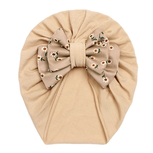 Detailed knit texture of beige baby turban featuring a large floral daisy bow decoration