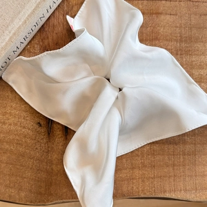 Close-up of white satin scrunchie with handmade pleated texture on a wooden tray