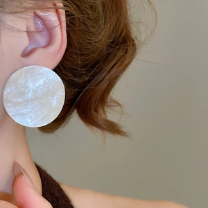 Close-up of large round acrylic stud earring with iridescent pearlescent texture worn by model