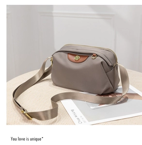 Detail of taupe oxford crossbody bag with brown leather trim and golden logo