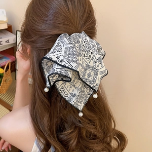Detail of a black and white paisley bow hair claw with pearl pendants on wavy brown hair