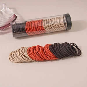 Set of high-stretch hair ties in orange, beige and dark brown with a clear storage tube