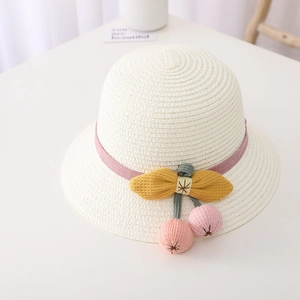 Close-up of white straw hat with pink ribbon, yellow bow and cherry pom-poms