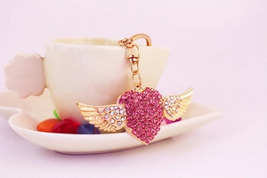 Close-up of pink rhinestone heart keychain with gold wings on white bowl edge