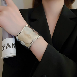 Close-up of wide wavy silver metal bracelet on a model wearing a dark blazer