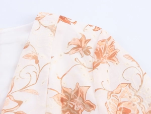 Dettaglio di motivi floreali ricamati e pizzo traforato su un abito lungo beige con scollo a V