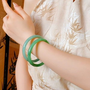 Detailed close-up of emerald green jade bangles worn on a wrist against a bamboo screen