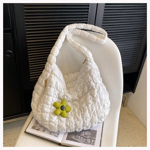 Detail of white quilted cloud tote bag with green flower charm on a white chair