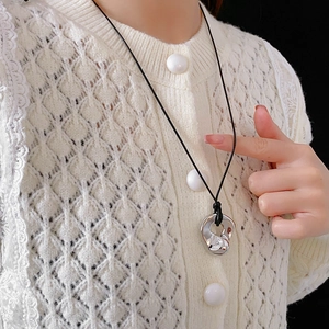 Detail of irregular silver fluid metal pendant with a black cord on a white knit cardigan