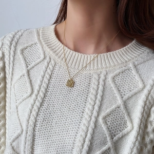 Detail of square gold lava texture pendant on a white chunky knit sweater for winter style
