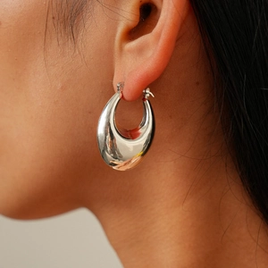 Close-up of chunky silver waterdrop hoop earrings on model showing glossy metallic finish