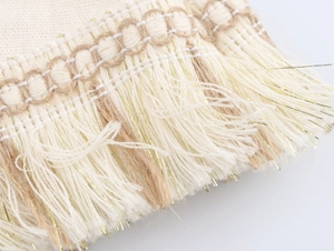 Detailed macro view of beige cotton fringe trim with interwoven metallic gold threads