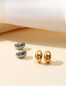 Detailed close-up of bean-shaped gold and silver earrings on a textured stone surface
