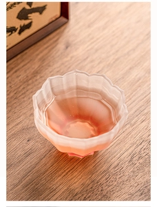 Close-up of frosted glass lotus tea cup with red tea on a rustic wooden table