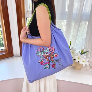 Detail of purple nylon tote bag with colorful embroidery and woven rope handle on model