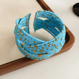 Détail d'un bracelet multicouche en perles de verre bleu ciel et or sur support bois