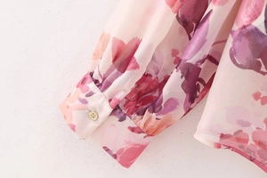 Dettaglio di polsini a punto smock e bottoni dorati su camicia rosa con stampa floreale