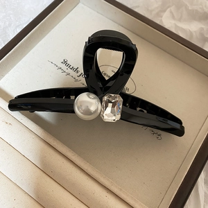Detail of a black glossy hair claw clip featuring a large pearl and rectangular gemstone