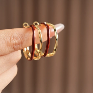 Detail view of gold and deep red enamel square hoop earrings held to show size and texture
