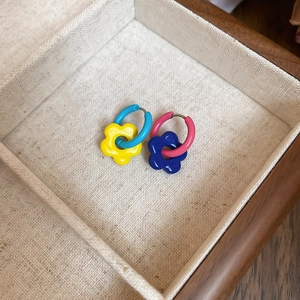 Detail of colorful asymmetric enamel flower earrings in a beige linen lined wooden box