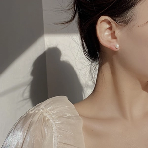 Close-up of elegant 6mm round pearl stud earrings on a model with artistic shadows