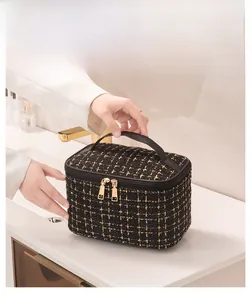 Detail of tweed makeup bag with gold zippers and handle on marble countertop