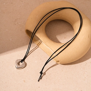 Detailed view of irregular silver heart pendant on black cord over neutral stone