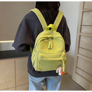 Detail of green corduroy backpack showing ribbed texture and cute pendant on a model