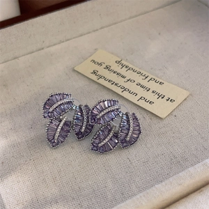 Close-up of purple zircon leaf earrings with white rhinestone accents on linen tray