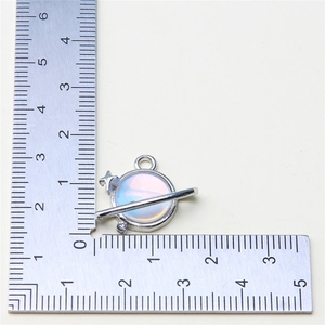 Detailed macro view of silver Saturn planet charm with translucent blue stone on a ruler