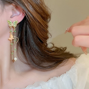 Detail of long tassel butterfly earrings with green stones and elegant white pearl drop