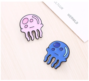 Close-up of cute pink and blue jellyfish enamel pins on a natural wood surface