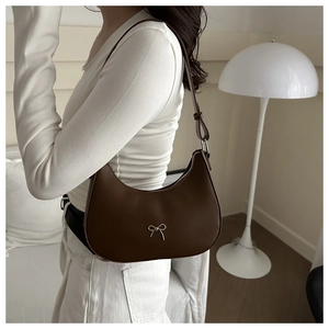 Detail of a brown crescent-shaped shoulder bag with silver bow accent on a model