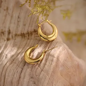 Detail of 18K gold-plated chunky hoop earrings with a polished mirror finish on wood
