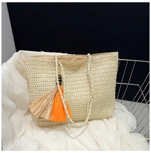 Detail of straw tote bag with colorful orange and brown fringe tassels on woven fabric