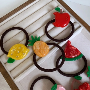 Bunte Haargummis mit Apfel-, Zitronen- und Ananas-Anhängern in einem Holztablett