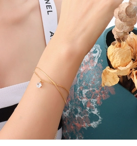 Détail d'un bracelet double chaîne doré avec un cristal étincelant sur le poignet d'une femme