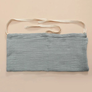 Close-up of sage green cotton double-pocket storage bag with cream ribbons for baby crib