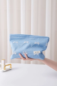 Dettaglio della trousse celeste con motivi a fiocco ed etichetta tessuta H&R